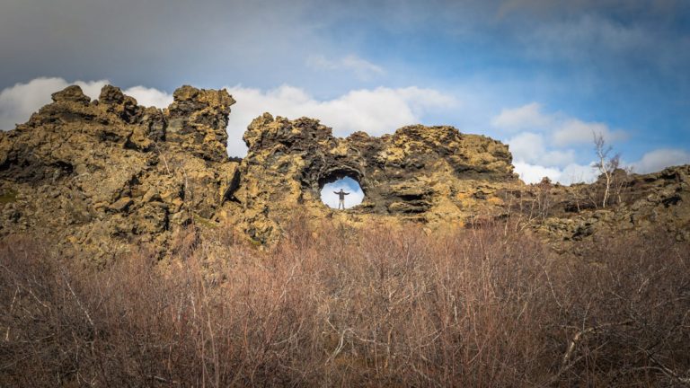 A traveler stands in a perfect circle cave in the rocks at Dimmuborgir Iceland
