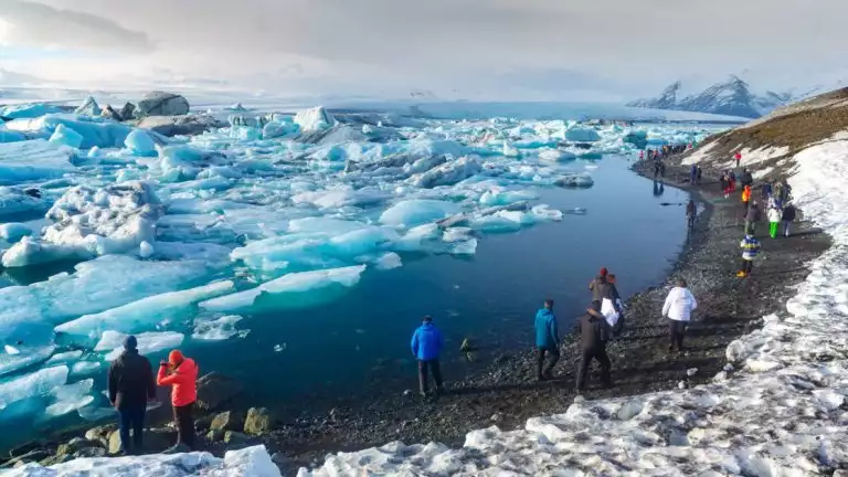 Jokulsarlon glacier lagoon in Iceland seen with travelers walking along the shoreline with the water filled with icebergs