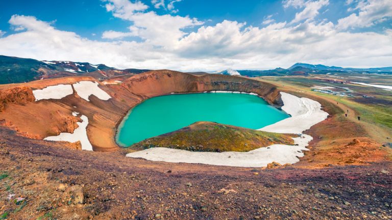 The vibrant blue Myvatn Lake seen with patches of snow around it in Iceland