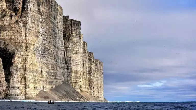 A giant cliff dwarfs a zodiac full of Northwest Passage expedition travelers at Prince Leopold Island