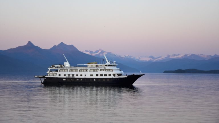 Safari Endeavour small ship with dark hull & white upper decks cruising through calm water at dusk on an Alaska winter cruise.