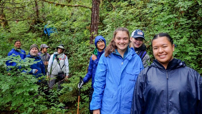 Alaska travelers hike through wet, dense green forest on the Glacier Bay National Park, Haines & Pelican cruise.