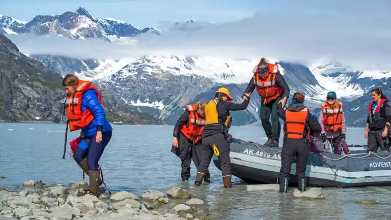 Alaska travelers exit a skiff boat onto a rocky beach on the Glacier Bay National Park, Haines & Pelican Cruise.