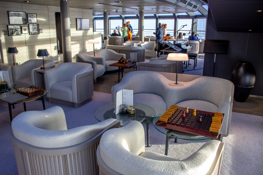 white upholstered chairs seated around glass coffee tables and board games in Observatory Lounge aboard Le Commandant Charcot. 