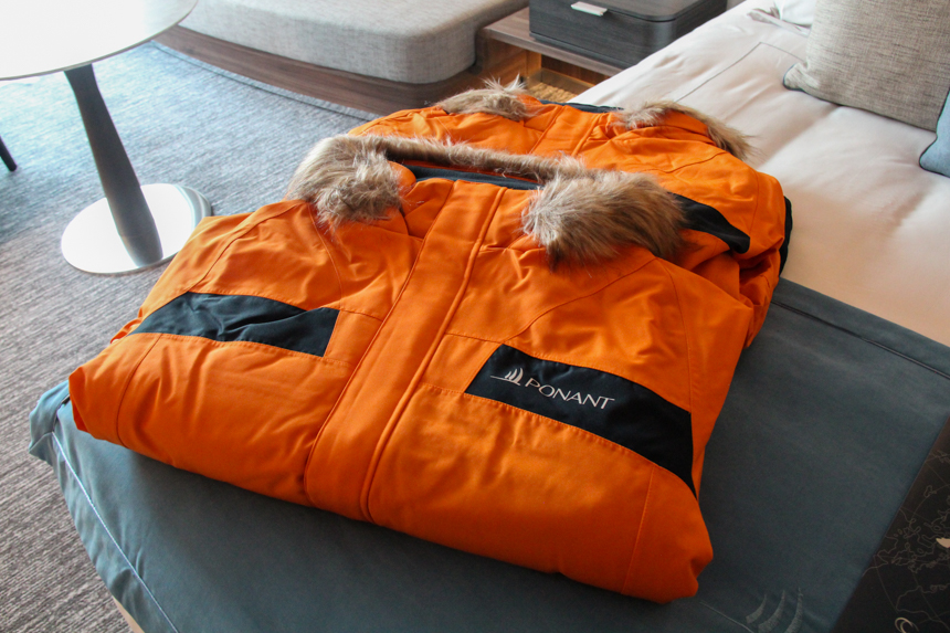 Thick warm orange Parka with fur lined hood folded on cabin bed given to arriving Charcot cruise guests. 