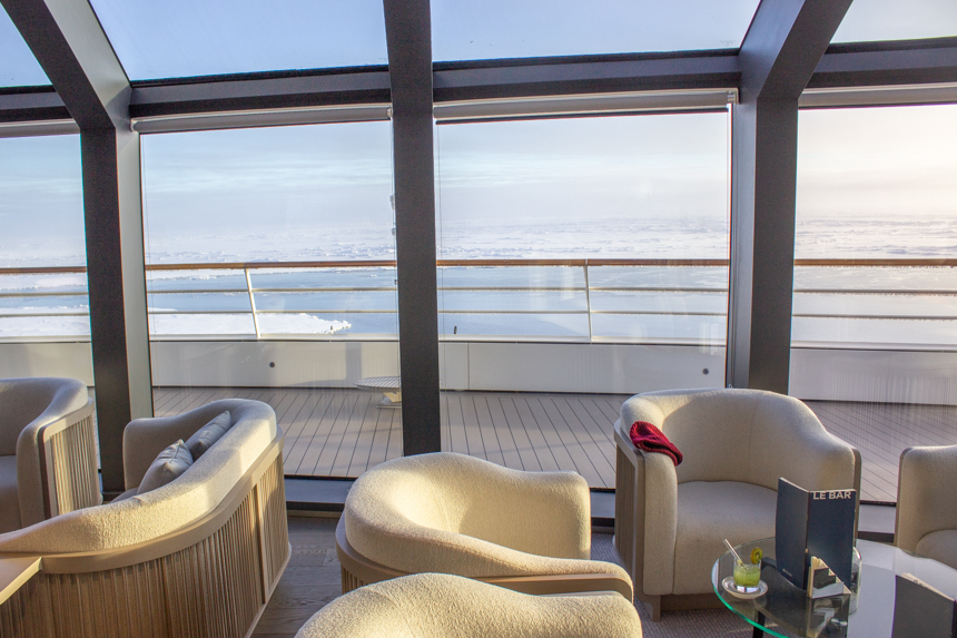 white upholstered chairs around glass coffee tables and games in Observatory Lounge with floor to ceiling windows. 