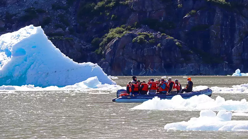 An inflatable skiff filled with guests in orange life jackets cruises between floating icebergs in Alaska. 