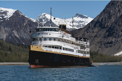 UnCruise Alaska 86-guest Wilderness Legacy with painted dark blue hull with a thin gold stripe and multiple white upper decks. 