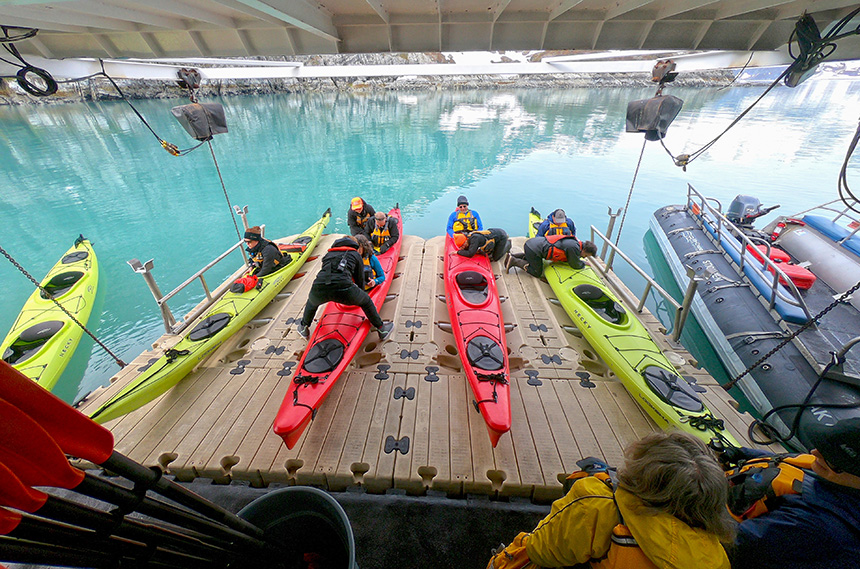 Guests enter 2 lime green and 2 red double kayaks from the EZ-dock floating kayak launching platform used by UnCruise Alaska ships