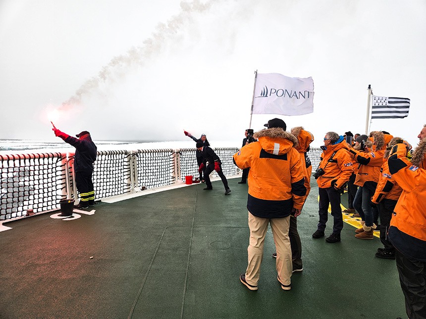 At the north pole guests gather at the ship bow to celebrate. Crew members hold flare guns and flags