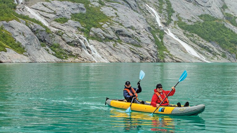 Two kayakers in a yellow kayak paddle in Nordfjord in the Norwegian Fjords with still blue glacial water