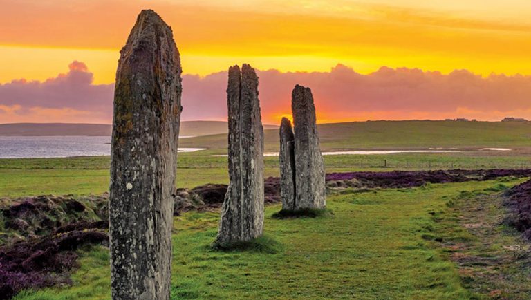 Three standing stones of the ancient and mysterious Ring of Brodgar underneath a dramatic sunset.