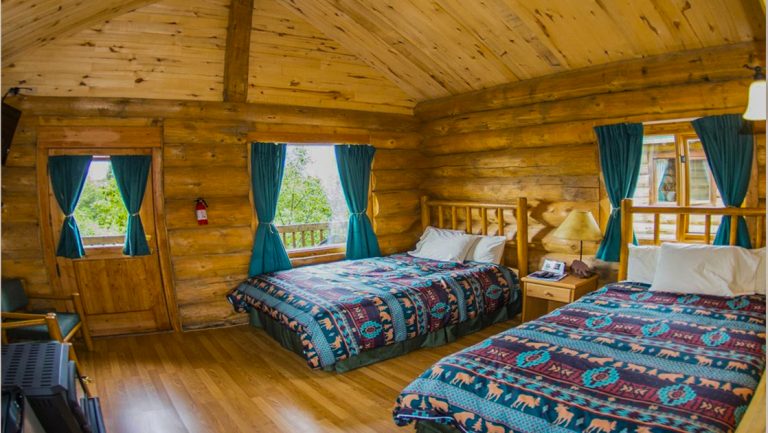 Inside guest log cabin at Alaska's Gold Creek Lodge in King Salmon, with 2 double beds, log furniture & bright windows.