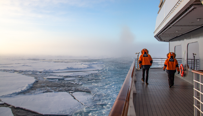 guests walk along the outer deck of ship as it pushes through an endless sea of white ice sheets