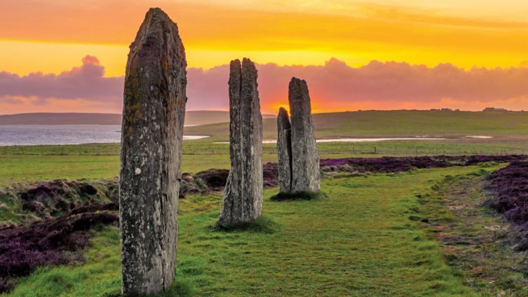 Three standing stones of the ancient and mysterious Ring of Brodgar underneath a dramatic sunset in Scotland