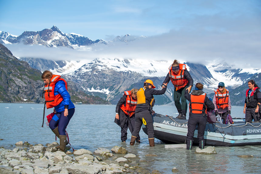 Alaska travelers exit a skiff boat onto a rocky beach on the Glacier Bay National Park, Haines & Pelican Cruise.