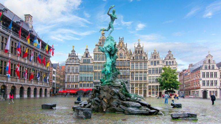Mint green statue & stone fountains encircled by multi-story, old-world, colorful stone & brick buildings in European city square.