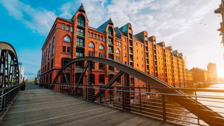 Modern wood & steel foot bridge over a canal beside tall, modern brick building at first light, seen on North Sea cruises.