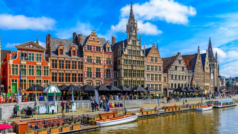 Canal with floating cafe & small boat parked beside waterfront old-world European brick buildings, seen on North Sea cruises.