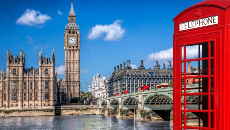 London symbols with Big Ben, red double-decker buses driving over an iconic bridge and red phone booth on a sunny day in England.