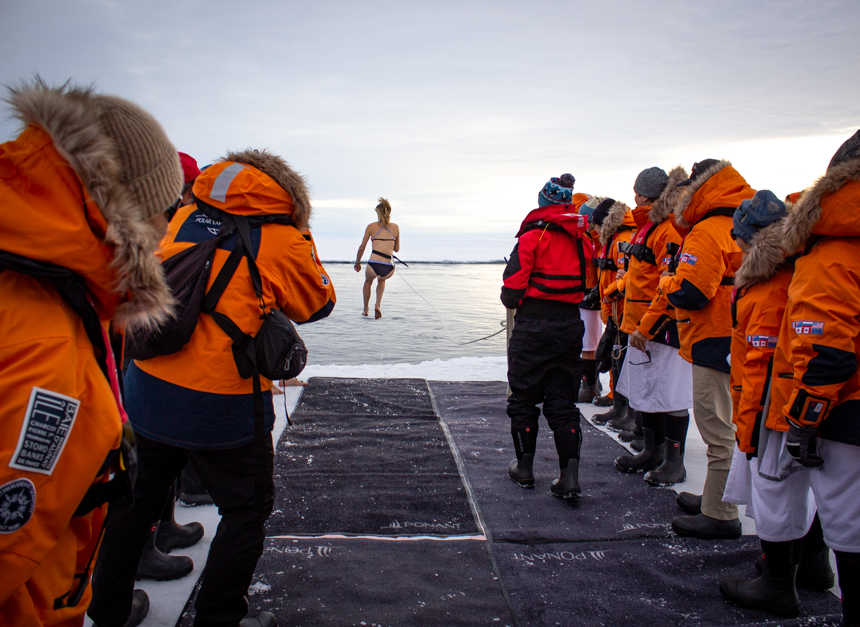 Crowd watches as girl jumps from ice edge into arctic ocean for Polar Plunge activity at North Pole. 