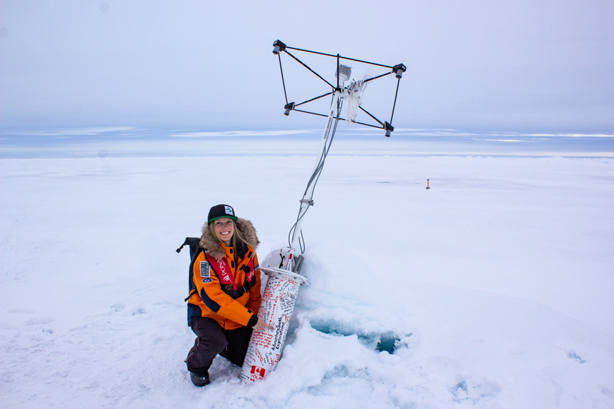 Girl at north pole poses with snow buoy used to measure snow and atmosphere data. 