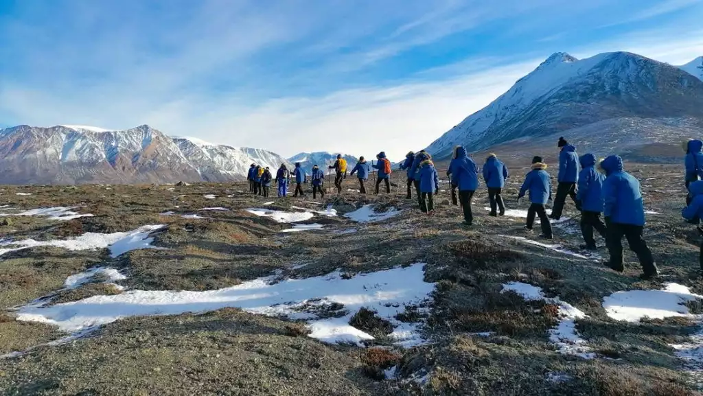 Group of Arctic travelers in blue jackets walk single file over gray tundra under blue sky on a Svalbard, Iceland & Greenland cruise.