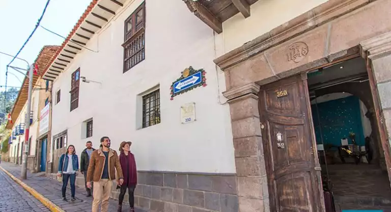 Peru travelers walk a city street to the front of XO Art House in Cusco, with a dark brown wood door & stone facade.