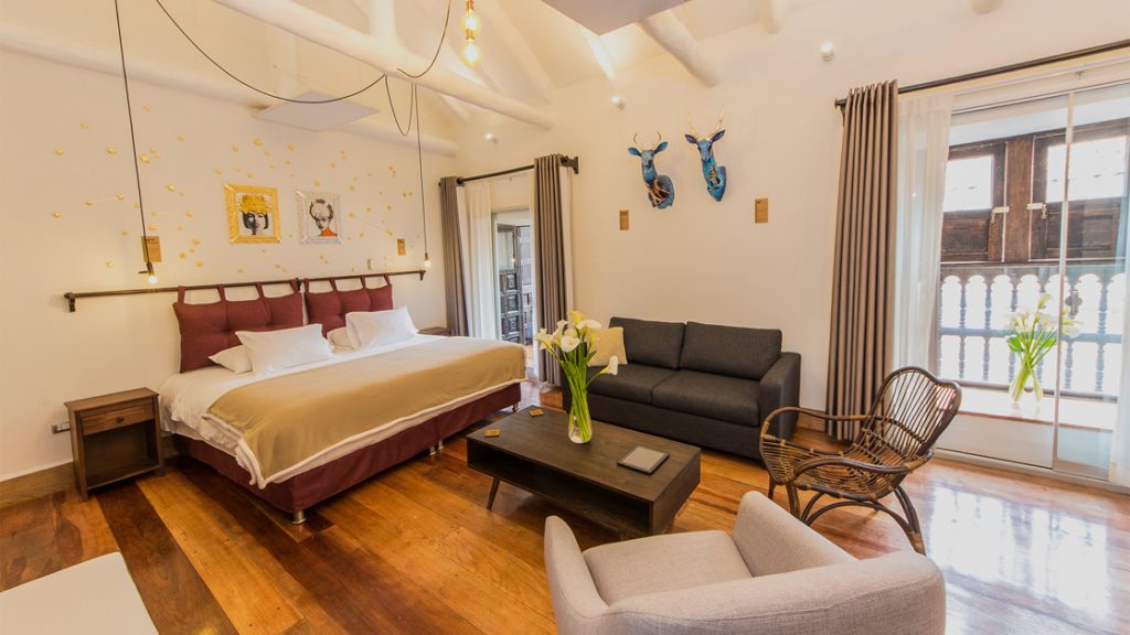 Superior Deluxe room at XO Art House Cusco with king bed, chair & love seat, coffee table, wood floor, large windows & local art.