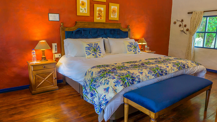 Wooden double bed with bench in floral sheets at Hacienda Pinsaqui with wood floors, window & red & white walls.