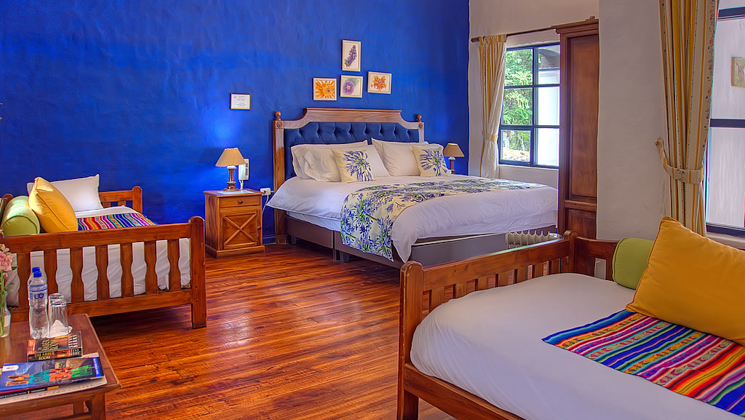Wooden double bed in floral sheets & 2 wooden daybeds at Hacienda Pinsaqui with wood floors, window & blue & white walls.