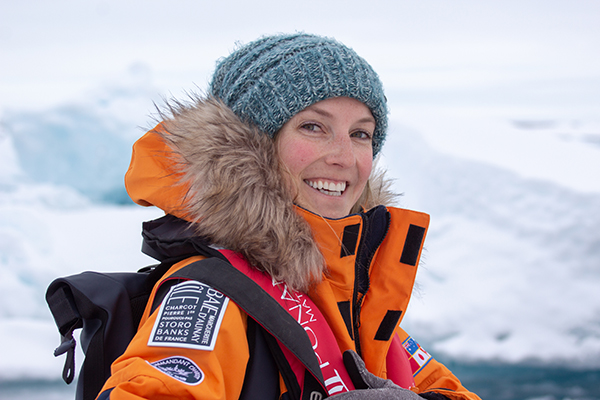 Female north pole traveler smiling wearing blue knit hat, orange parka with fur hood.