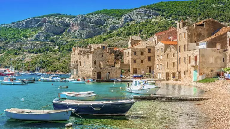 Seafront scenic view at Komiza in South of Croatia, Mediterranean, with dinghy boats, seaside brick buildings & green hills.