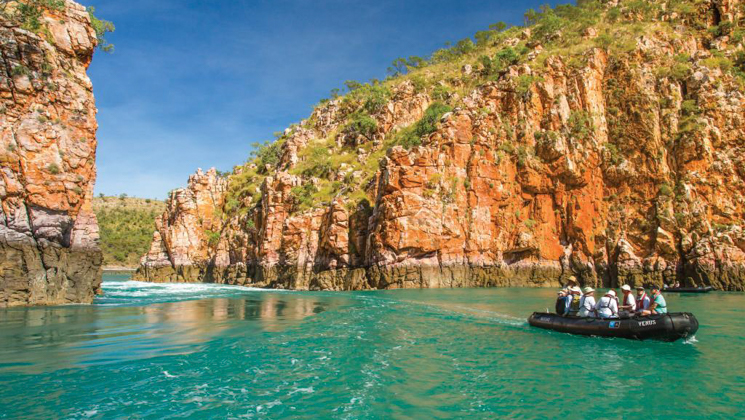 Kimberley travelers take a Zodiac cruise through turquoise water by red canyon walls at Horizontal Falls, Northwest Australia.