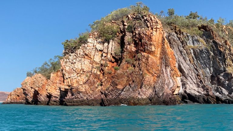 Tall island with red & white rock & small green trees growing atop it sits in turquoise water, seen on a Kimberley Expedition.