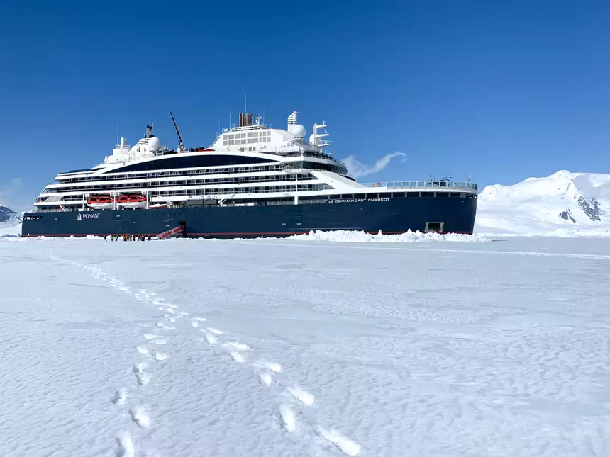 Blue and white ship, Le Commandant Charcot, parks in thick ice sheet as guests explore on foot during Bellingshausen Sea voyage