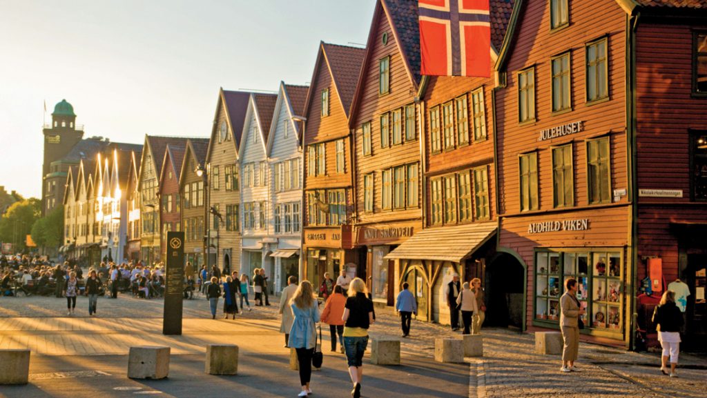 Bergen, Norway at sunset with multicolored buildings by pedestrian walkway with travelers on a Legendary Northern Isles cruise.