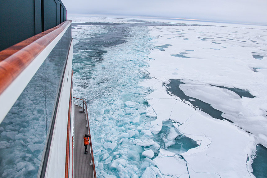 A lone photographer stands on a ship deck pointing their camera out toward the sea ice