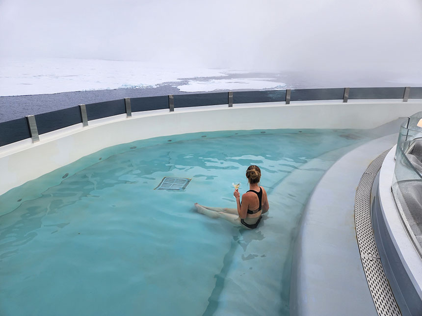 A traveler sits in a heated pool with a drink on her ship at the North Pole