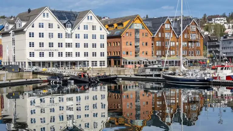 Reflections of water and boats docked in front of a row of colorful buildings in Norway.