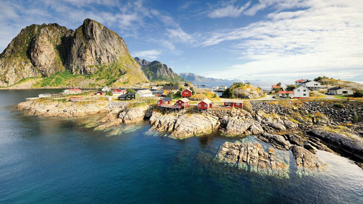 Remote village of small colorful homes sits atop rocky island with mountain in the background on a sunny day.