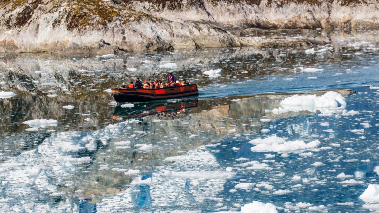 Zodiac cruise with Southern Patagonia travelers goes through calm water with floating bergy bits of ice by rocky shoreline.