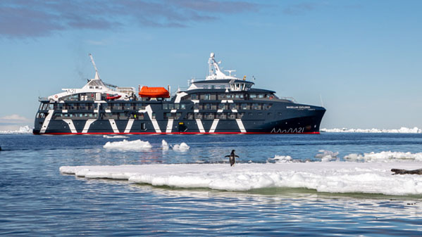 The Antarctic expedition ship Magellan Explorer seen on its starboard side with a flat iceberg and penguin in the foreground