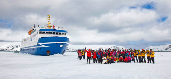 A group of Antarctic cruise passengers stands in front of their small ship docked on ice