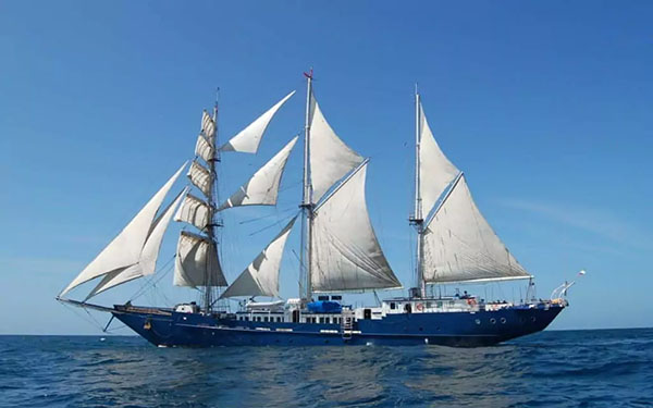 The full port side of blue hulled Mary Anne Galapagos cruise ship with its white sails all up
