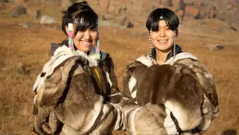 Arctic Inuit boy & girl post for a photo in animal fur coats & beaded headbands while standing among golden tundra.