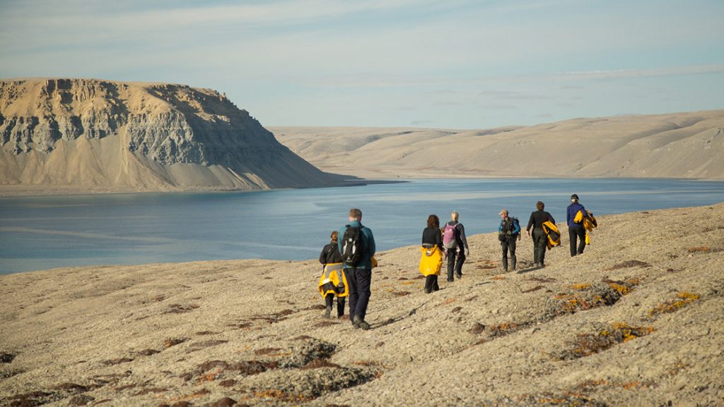 Travelers on a Northwest Passage small ship cruise walk along a sandy riverbank in a barren landscape on a hazy day.