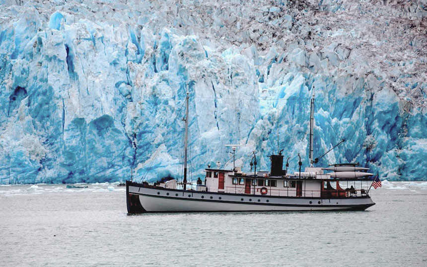 Alaska small ship Catalyst cruses in front of a jagged icy blue and white glacier in Alaska  