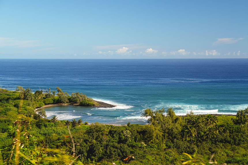 The magnificent coastline of Hawaii, green lush rainforest land leads to coves and beaches white waves blue ocean and blue sky