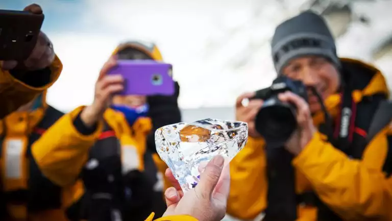 Man & woman in yellow coats hold camera & phone up to photograph a small chunk of ice on a Spitsbergen Photography cruise.